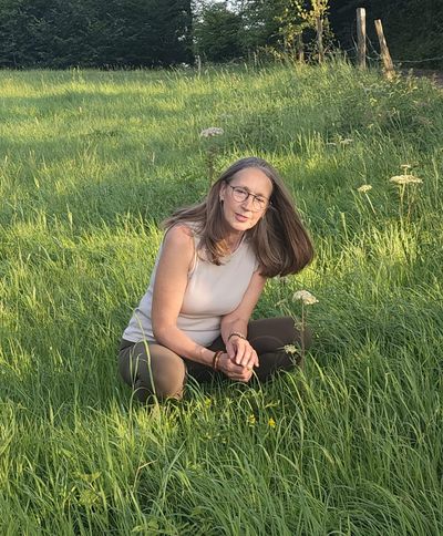 Heike kniet im hohen Gras und betrachtet blühende Wildkräuter am Wegesrand